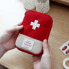 A hand holds a red portable mini first aid kit organizer bag with a white cross emblem on a light background.