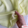 Close-up of pale yellow silk chiffon fabric being draped and folded by a hand.