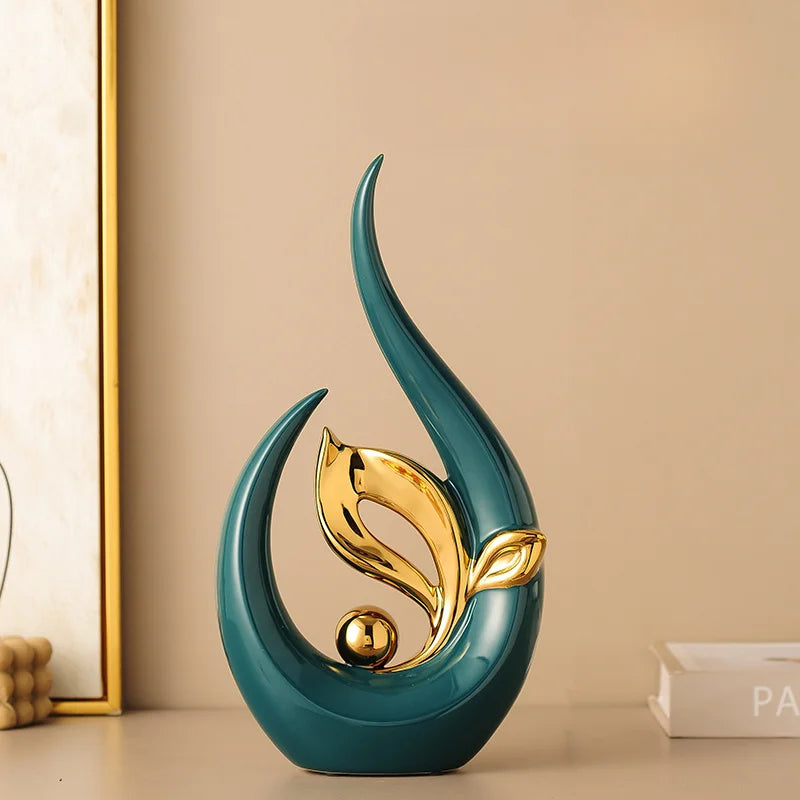 A teal ceramic sculpture with a gold leaf design stands on a light surface.