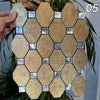 A hand holds a square mosaic tile made of beige and silver tiles, set against a green plant background.