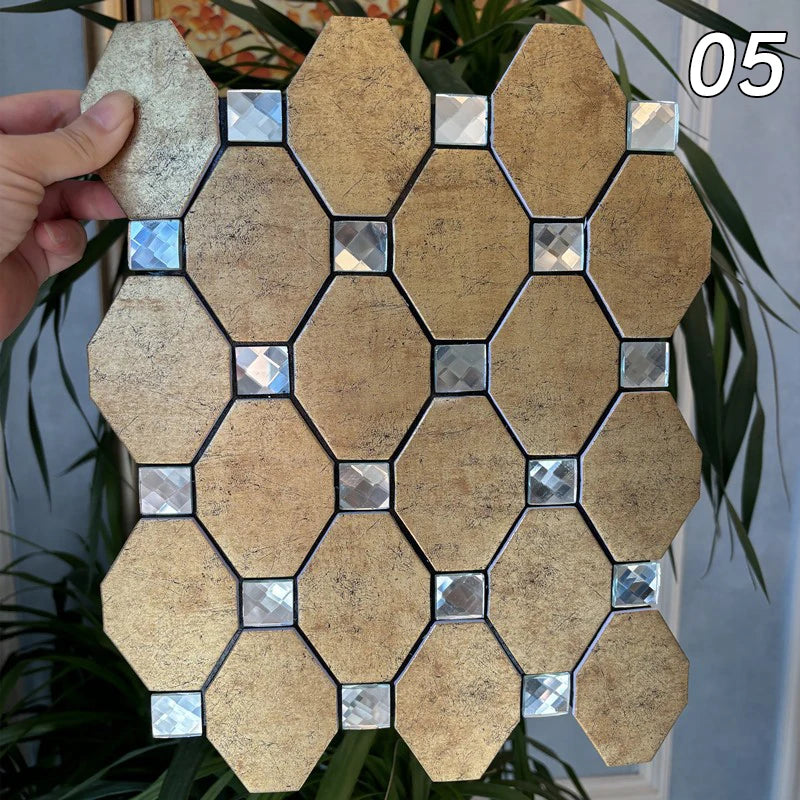 A hand holds a square mosaic tile made of beige and silver tiles, set against a green plant background.