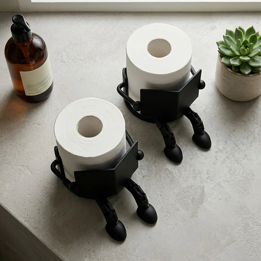A black, human-shaped freestanding toilet paper holder stands next to a roll of white toilet paper and an oil bottle on a lig