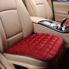 A close-up view of a plush red seat cover placed on the seat of a beige car interior.