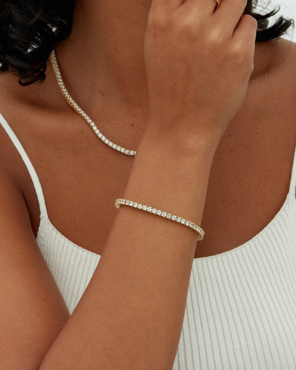 A close-up of a woman wearing a delicate gold plated tennis bracelet on her wrist.
