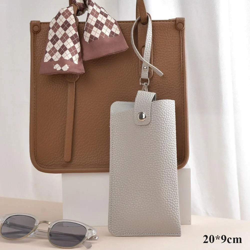 A tan leather handbag with a checkered fabric strap and a light gray PU leather glasses case hanging from it.