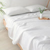 Eine weiße gesteppte Decke ist über einem Bett drapiert, mit einem weißen Kissen und einer Vase mit Grünzeug sichtbar.