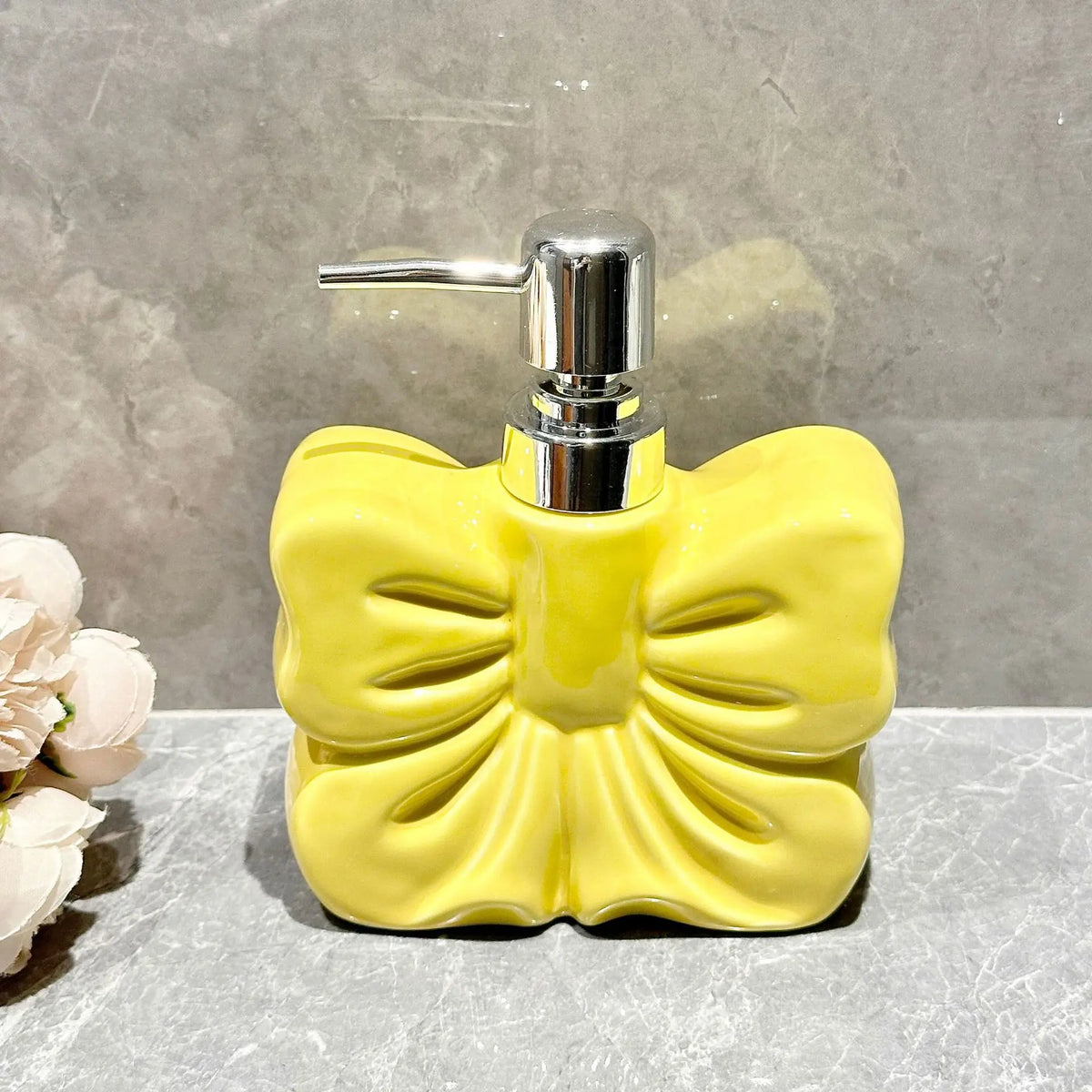 A yellow ceramic pump dispenser with a silver pump mechanism sits on a gray surface.