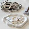 A white cloud-shaped jewelry tray holds various silver and pearl necklaces and rings.