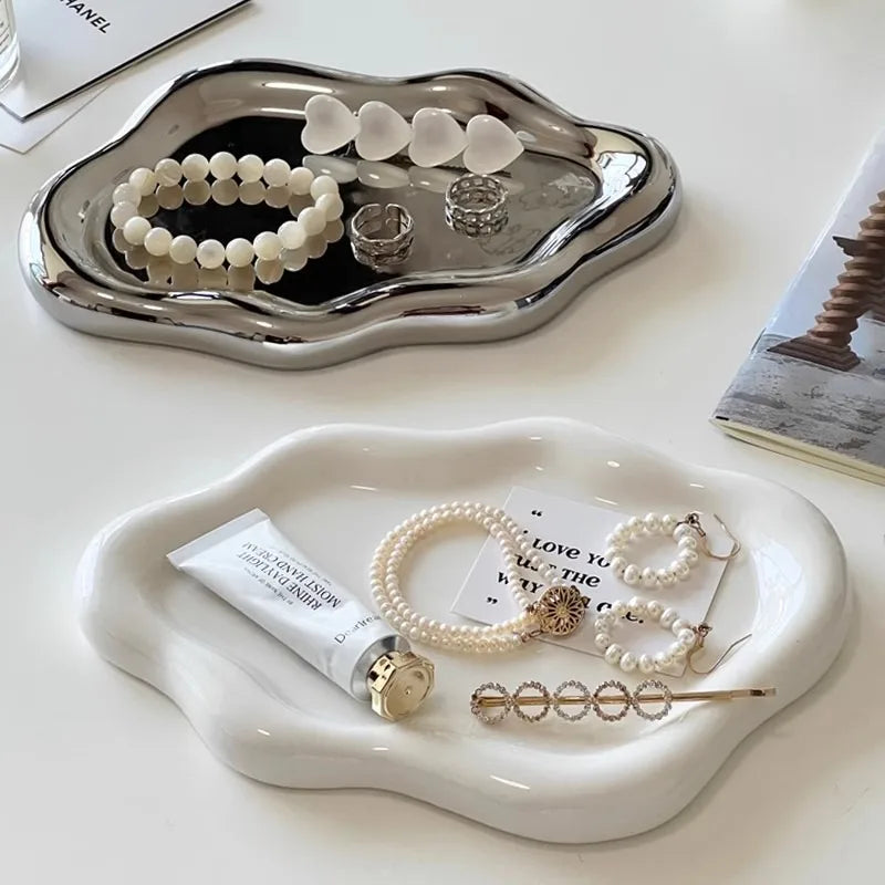 A white cloud-shaped jewelry tray holds various silver and pearl necklaces and rings.