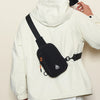 A white jacket features a black water-resistant nylon chest sling bag with an orange detail.