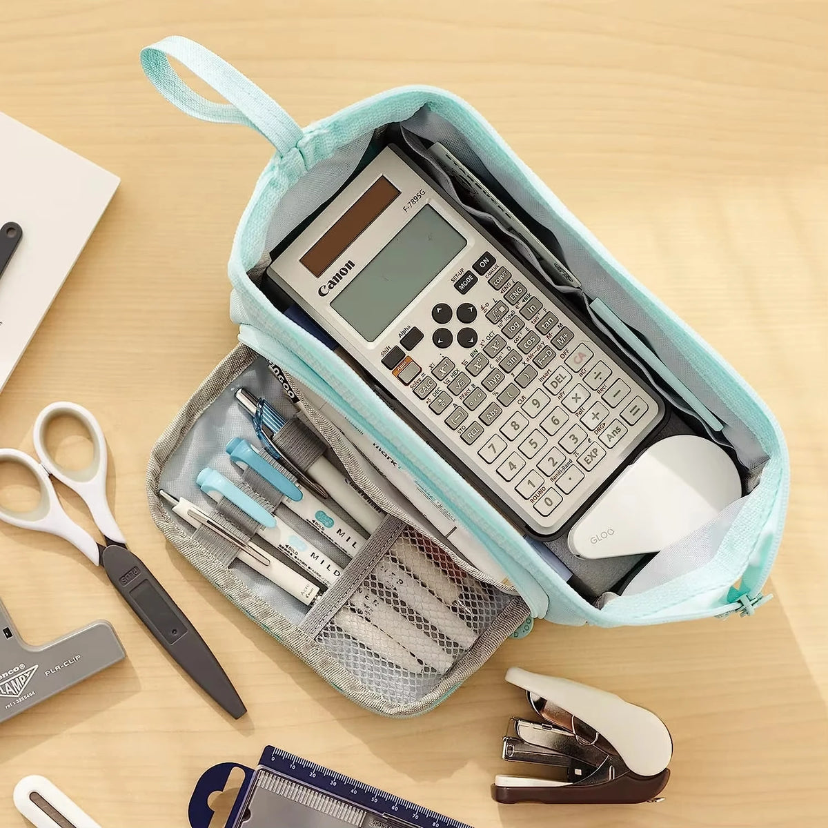 A light blue pencil case is open, showing a Canon calculator and various pens and scissors inside.