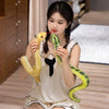 A young woman is holding a yellow snake plush toy and a green snake plush toy.