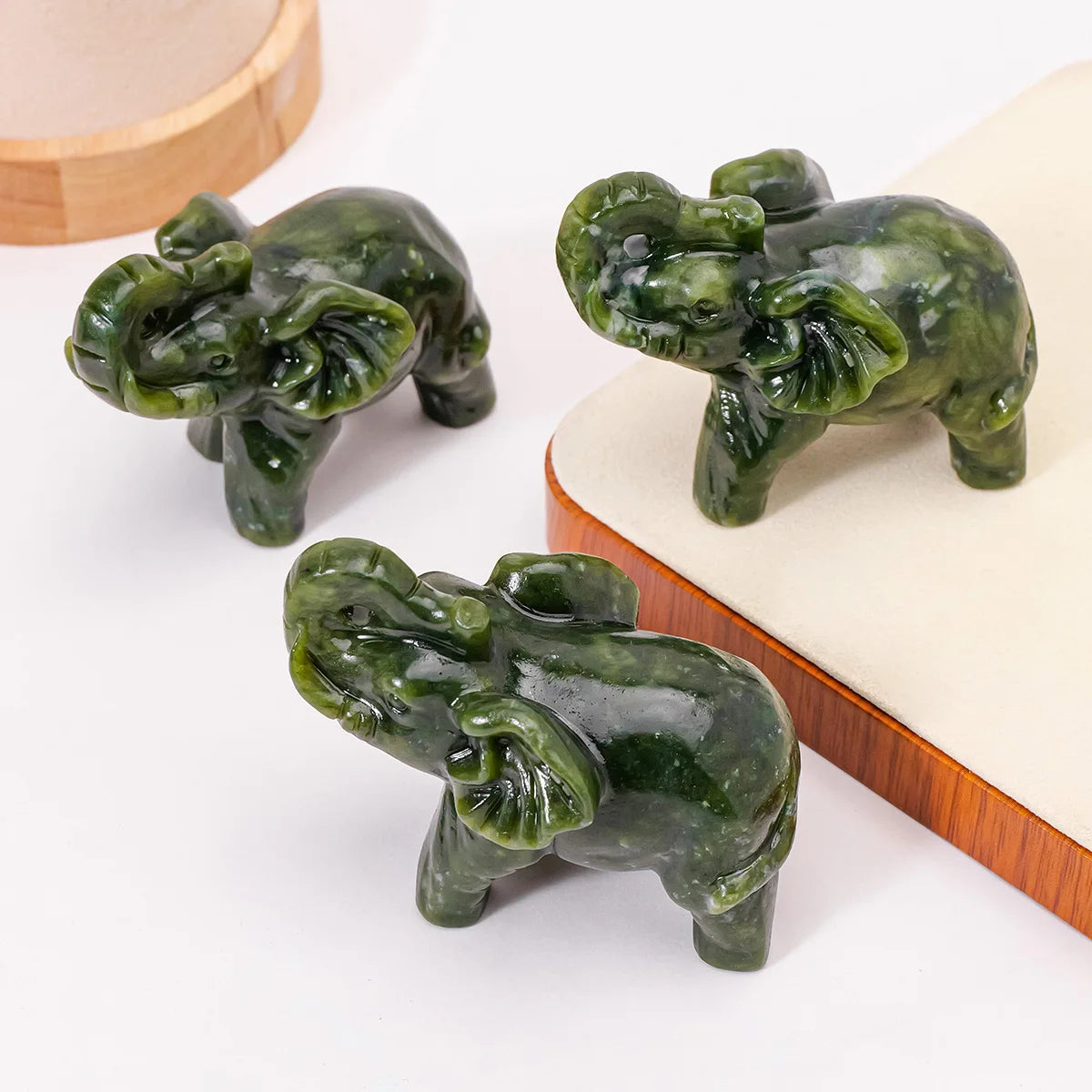 Hand-carved natural jade elephant statue in green resting on a light wooden surface.