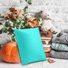 A teal padded bubble mailer resting on a wooden surface next to a stuffed bear and autumn leaves.