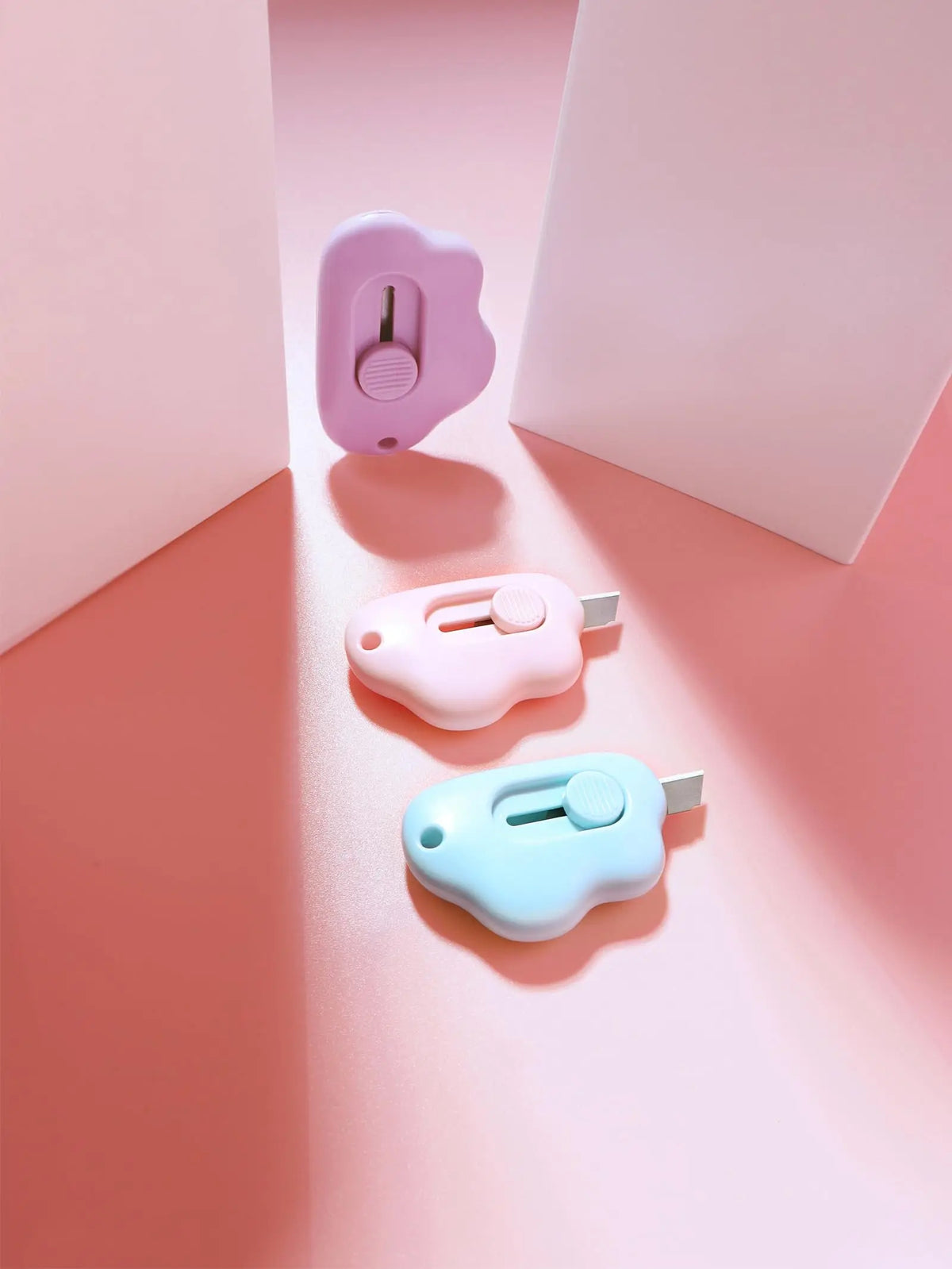 Three cloud-shaped retractable letter openers in purple, pink, and light blue displayed on a soft pink background.