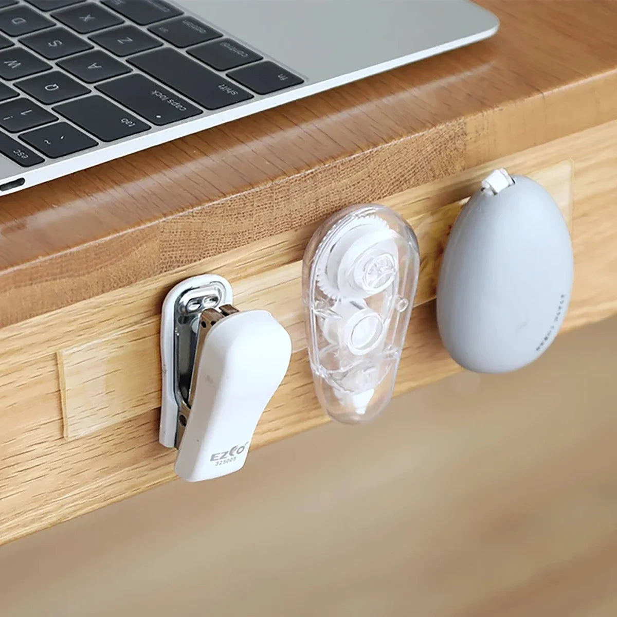 A white adhesive tape dispenser and roll are placed on a wooden desk next to a laptop.