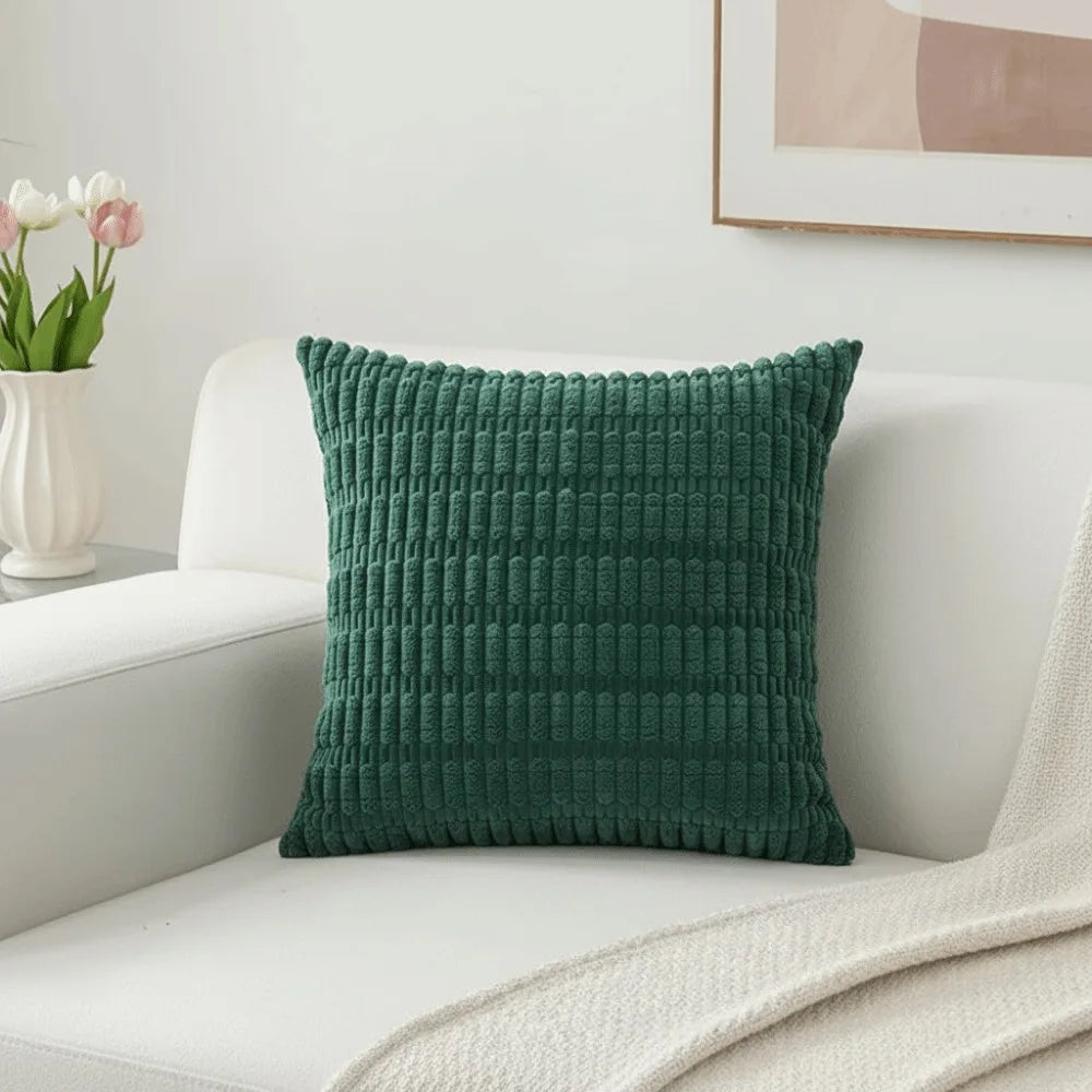 A dark green corduroy pillowcase with a textured, striped velvet design resting on a white sofa.