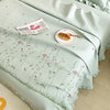 A light mint green quilted bedspread featuring embroidered floral patterns and a small plate with a croissant.