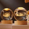A laser engraved crystal ball night light with a golden glow resting on a wooden base.