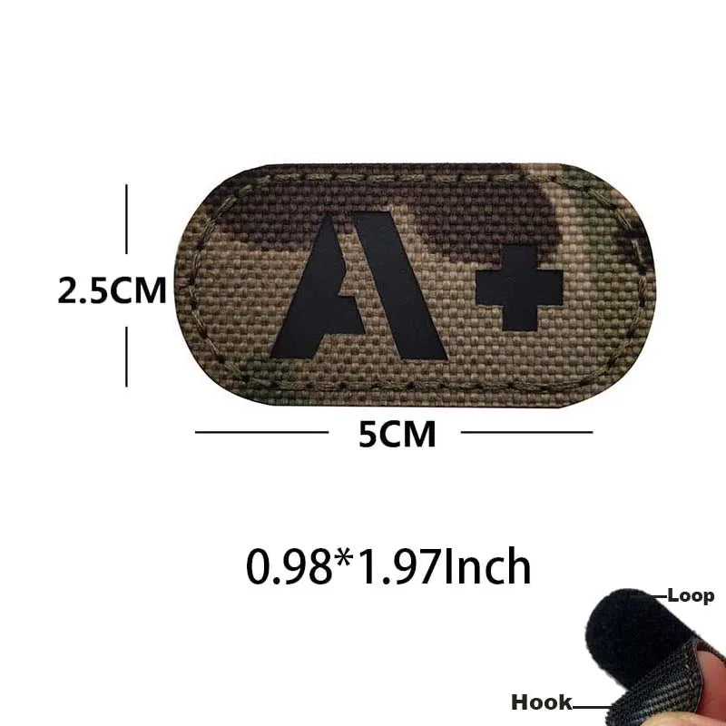 A dark camouflage patch with a black letter A and plus sign, measuring 2.5cm by 5cm, featuring a hook and loop backing.