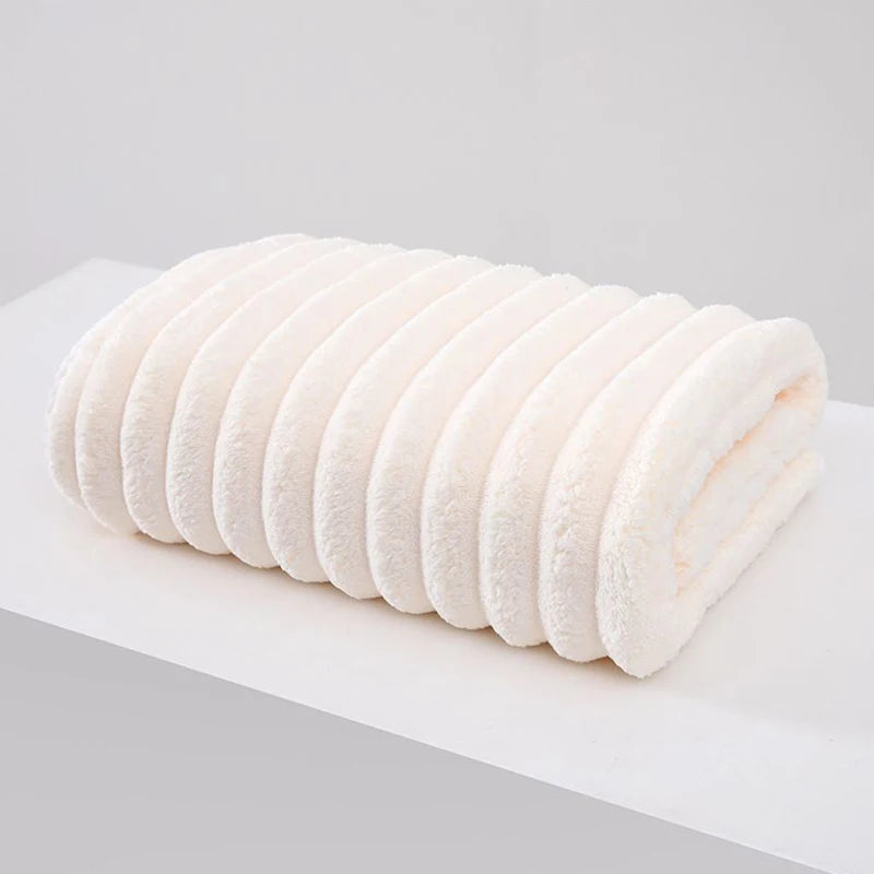 A roll of white plush coral velvet bath towels stacked horizontally on a white surface.