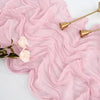 Pink sheer fabric draped with dried flowers and gold-toned utensils on a white surface.