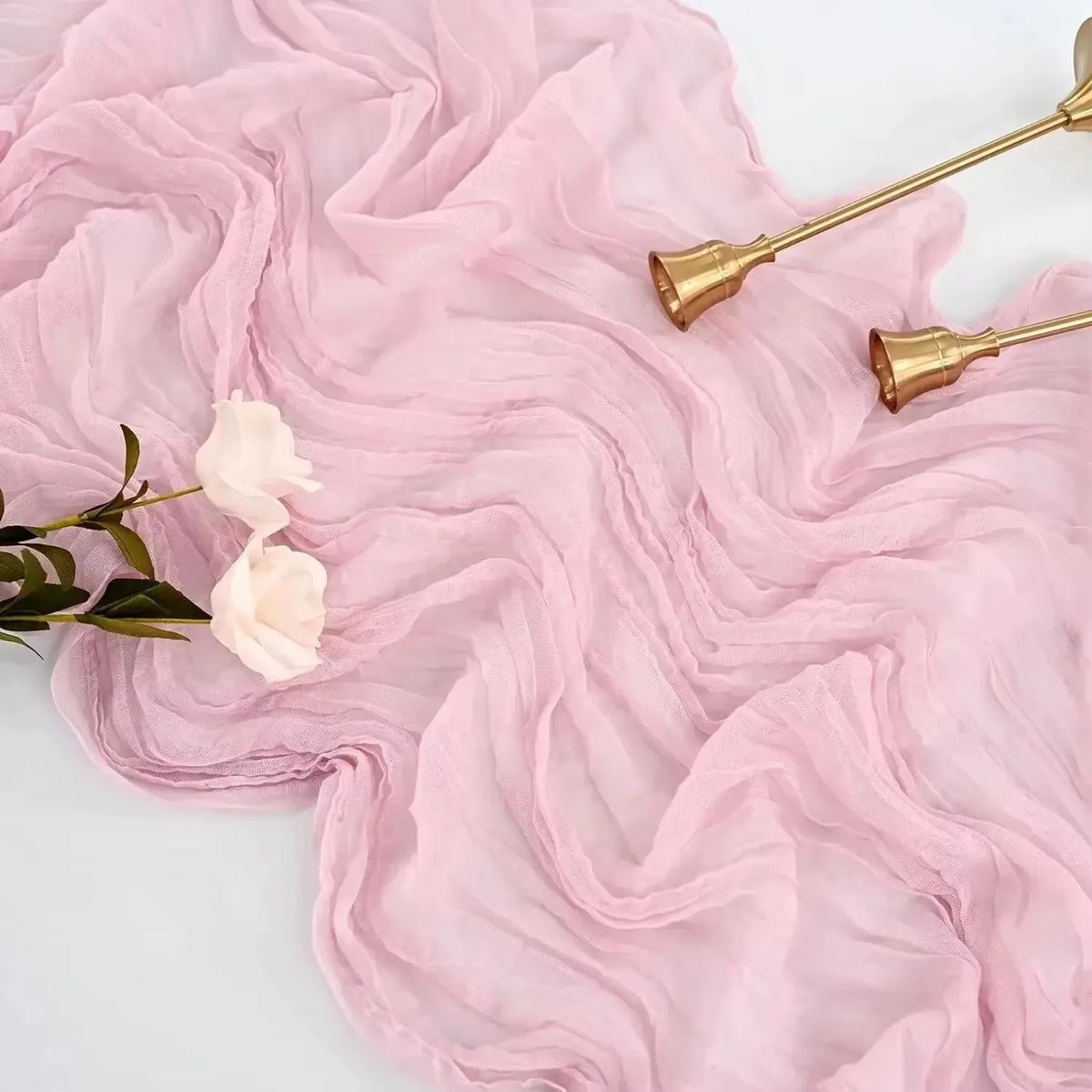 Pink sheer fabric draped with dried flowers and gold-toned utensils on a white surface.