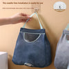 A hand is installing a wall-mounted mesh garbage bag holder with a hook onto a beige wall.