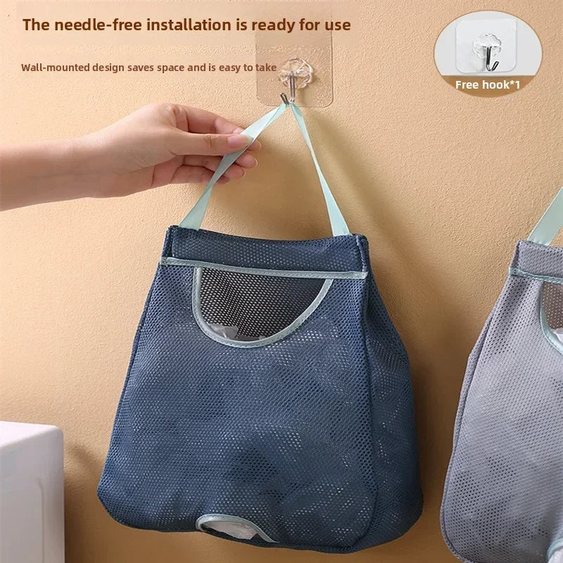 A hand is installing a wall-mounted mesh garbage bag holder with a hook onto a beige wall.