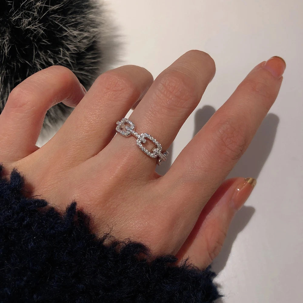 A hand wearing a geometric sterling silver stackable ring with cubic zirconia on a finger against a white background.