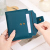 A teal leather bifold wallet with a card slot is held by a person on a white surface.
