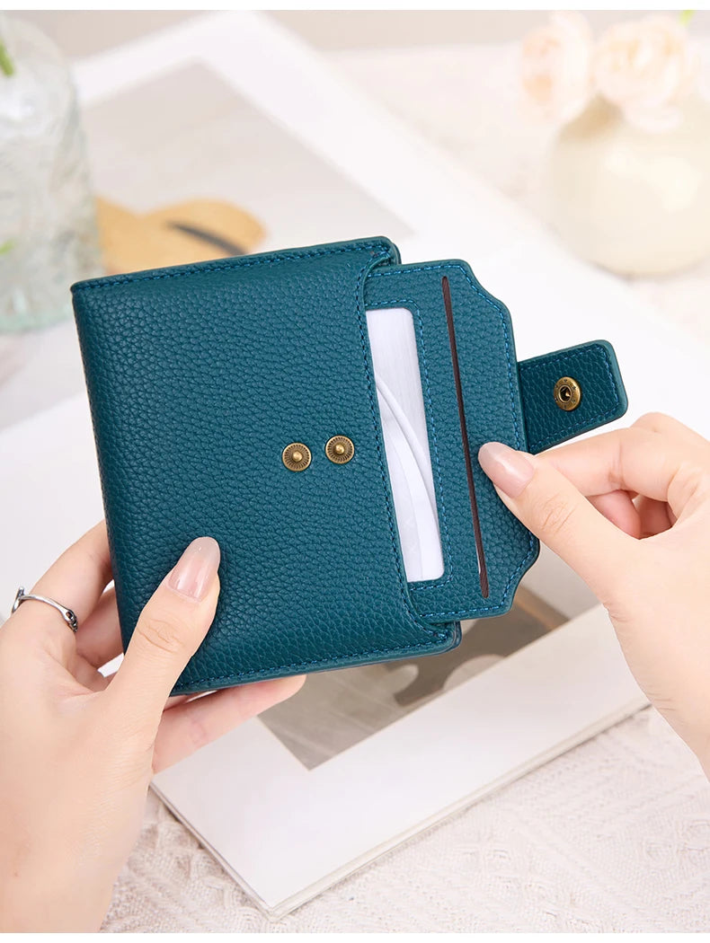 A teal leather bifold wallet with a card slot is held by a person on a white surface.