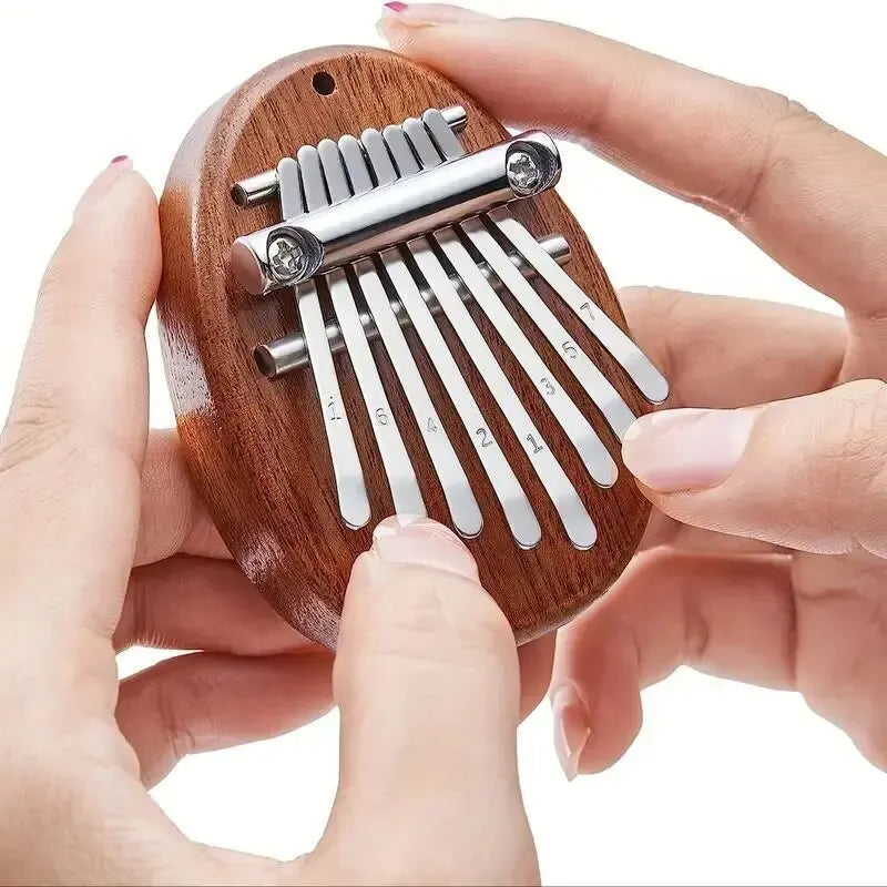 A hand holds an 8-key wooden kalimba thumb piano with metal tines.