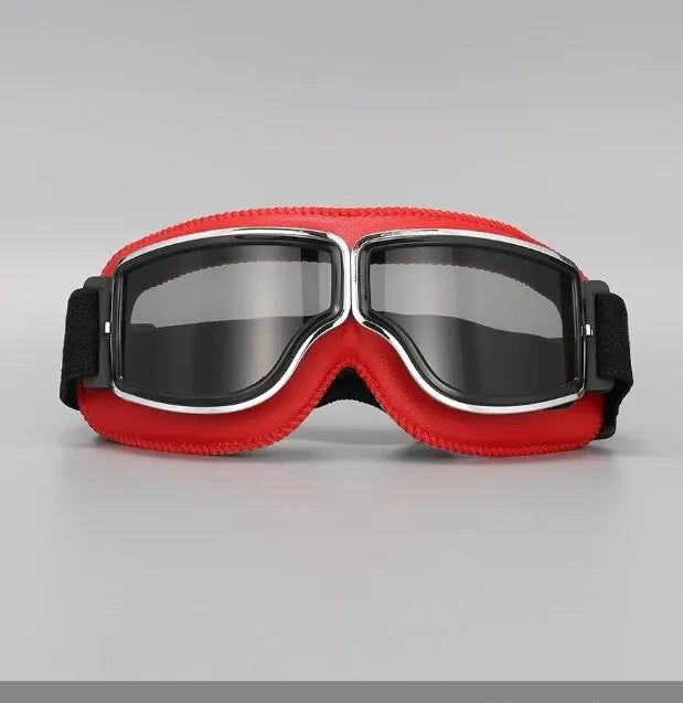A pair of red and black retro foldable motorcycle goggles with a clear lens.