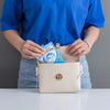 A person is holding a beige pouch containing disposable toilet seat covers.