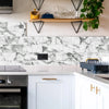 A kitchen backsplash featuring white marble self-adhesive tiles with gray veining and black metal shelving.