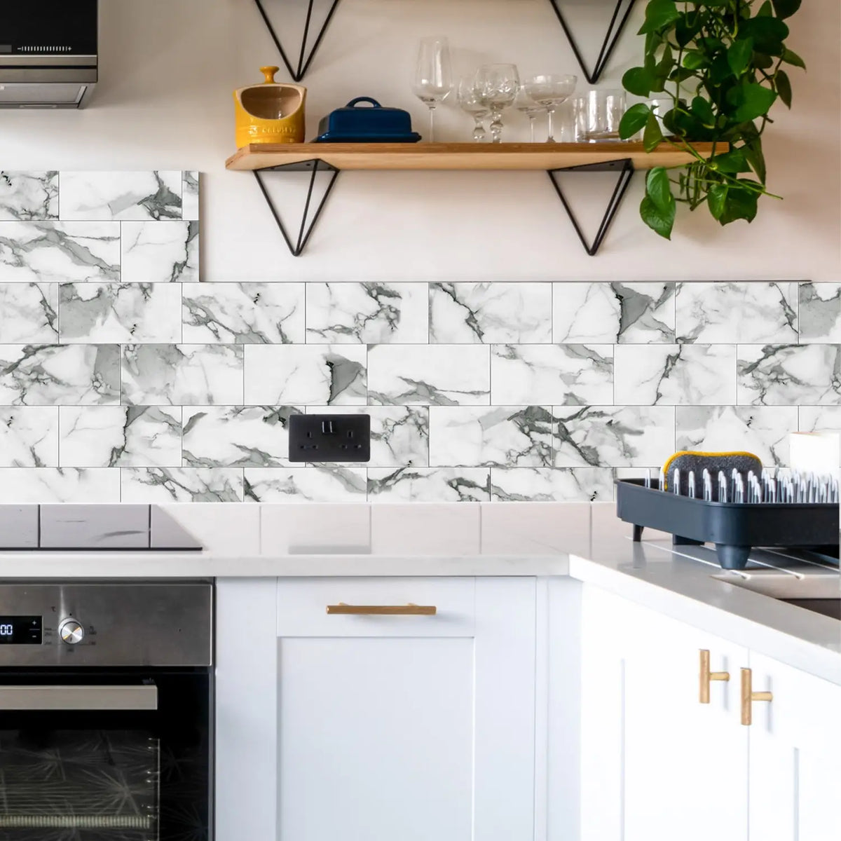 A kitchen backsplash featuring white marble self-adhesive tiles with gray veining and black metal shelving.