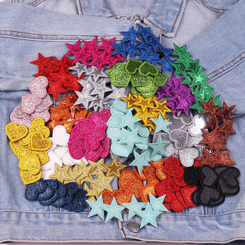 A collection of colorful glitter heart and star iron-on embroidered patches in various shades arranged on a denim fabric.