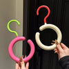 A hand holds a pink and green Nordic wall-mounted hat and scarf organizer hook against a dark door.