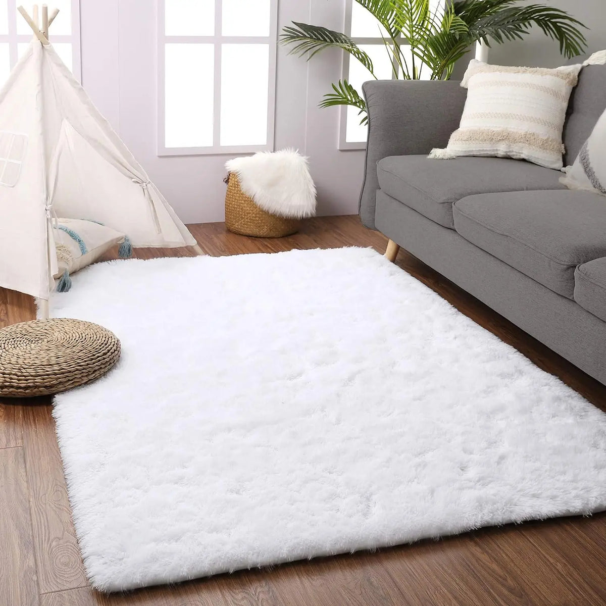 A fluffy white rug with a natural fiber border is placed on a wooden floor next to a gray sofa.