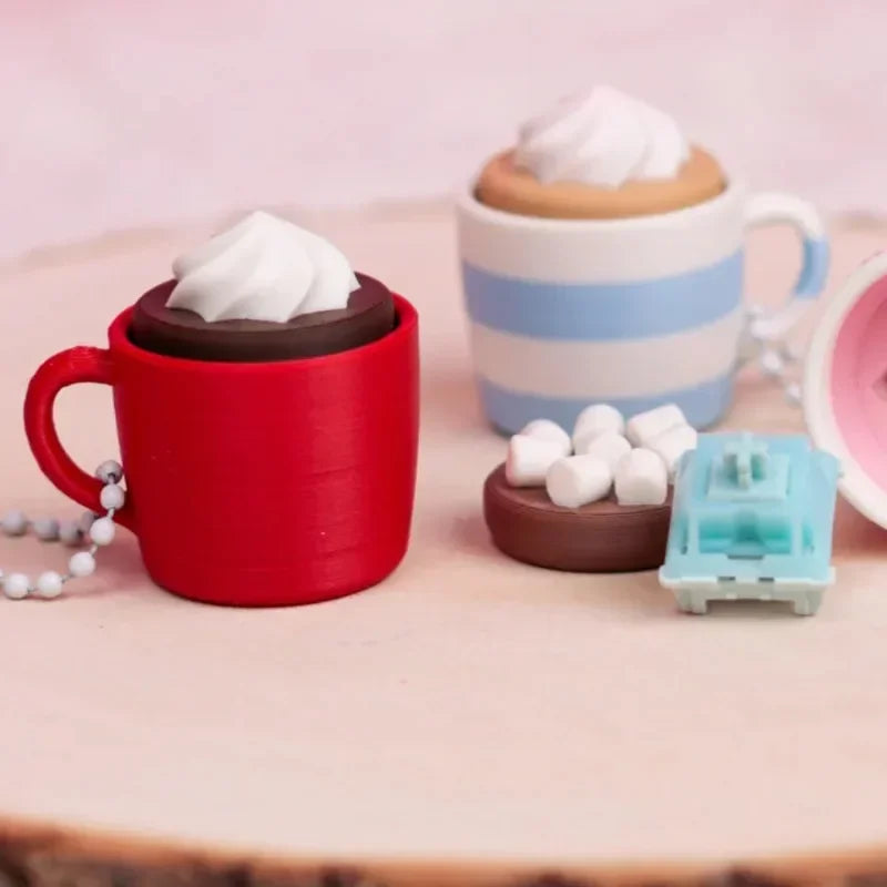 A red mug, a white whipped cream topping, and a light blue striped mug are displayed next to a teal fidget toy.