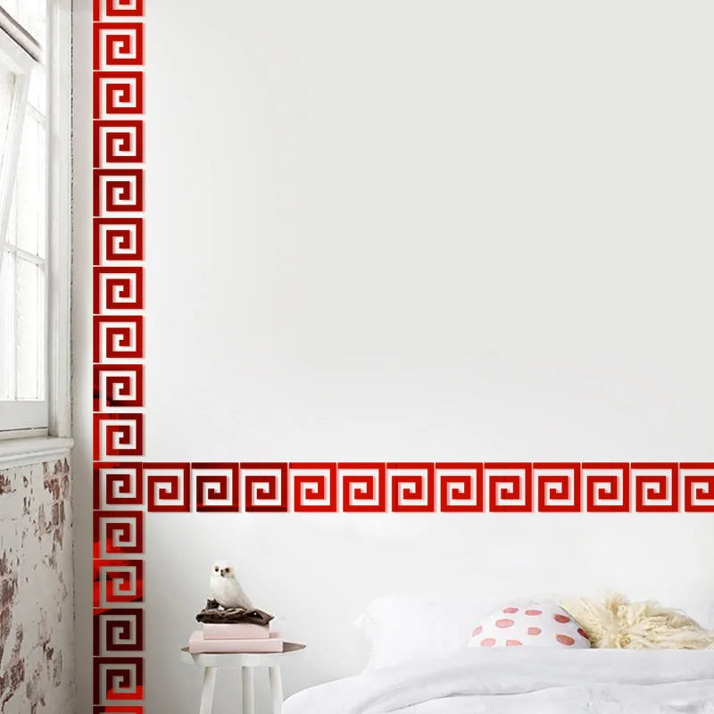 A white wall with red geometric mirror stickers decorating a vertical border and a horizontal band above a bed.