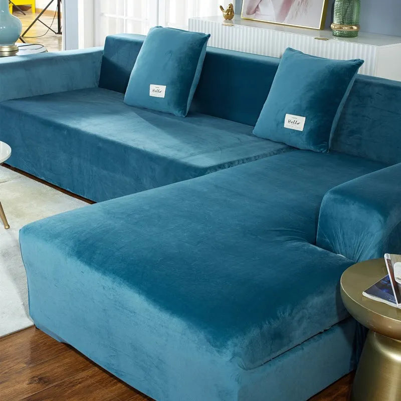 A deep teal plush velvet elastic sofa cover with light blue accent pillows on an L-shaped sofa.