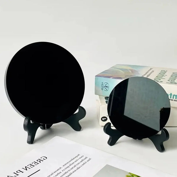A black obsidian scrying mirror crystal resting on a stand next to its packaging box.