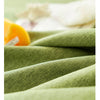 A close-up of a textured olive green farmhouse tablecloth with white cotton tassels and a yellow object.