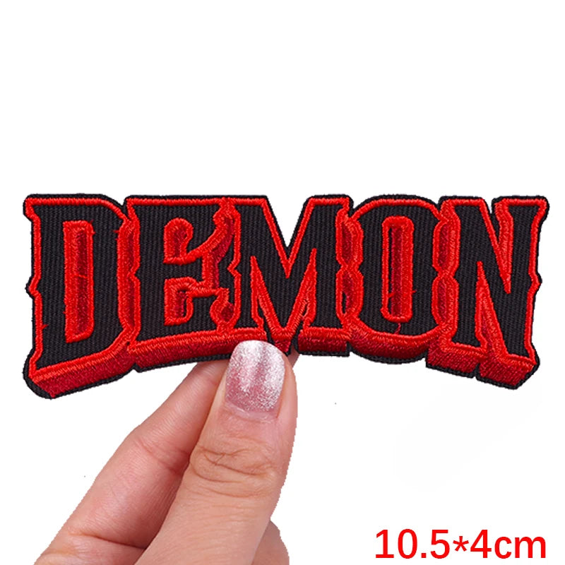 Red embroidered text patch spelling DEMON shown being held by a hand