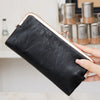 A black leather wallet with a gold-toned clasp is held by a hand against a light background.