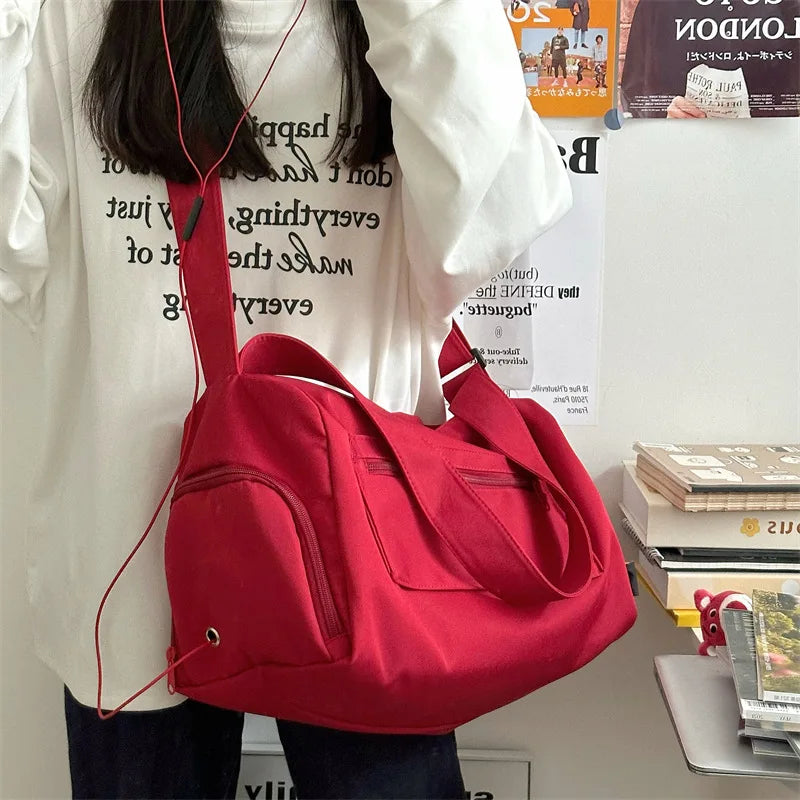 A bright red large canvas travel tote bag with a strap is displayed against a white shirt.