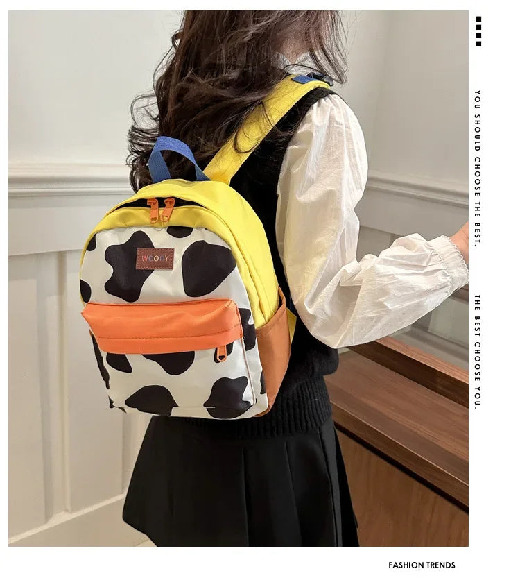A woman is shown from the back wearing a yellow and black cow print backpack with orange accents.