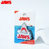 A rectangular packaging for a Jaws collectible enamel pin featuring a shark design.